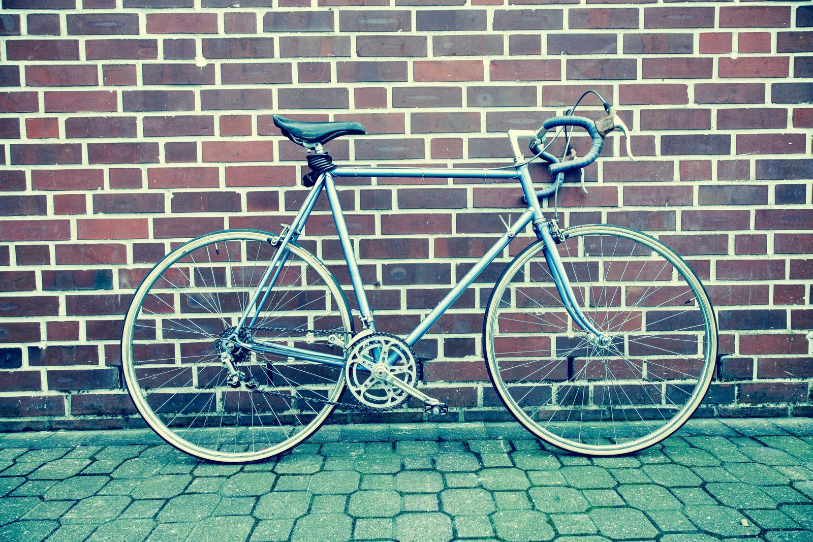 A classic racing bicycle leaning against a brick wall on a paved street.